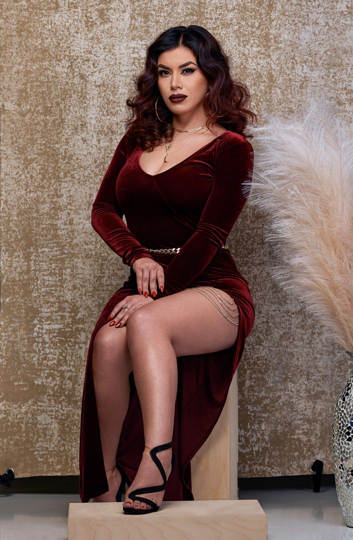 Elegant pose in burgundy velvet dress with decorative feathers.
