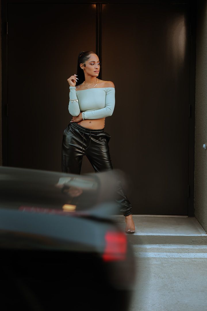 Modern fashion photo of person in off-shoulder crop top and leather pants in parking garage.