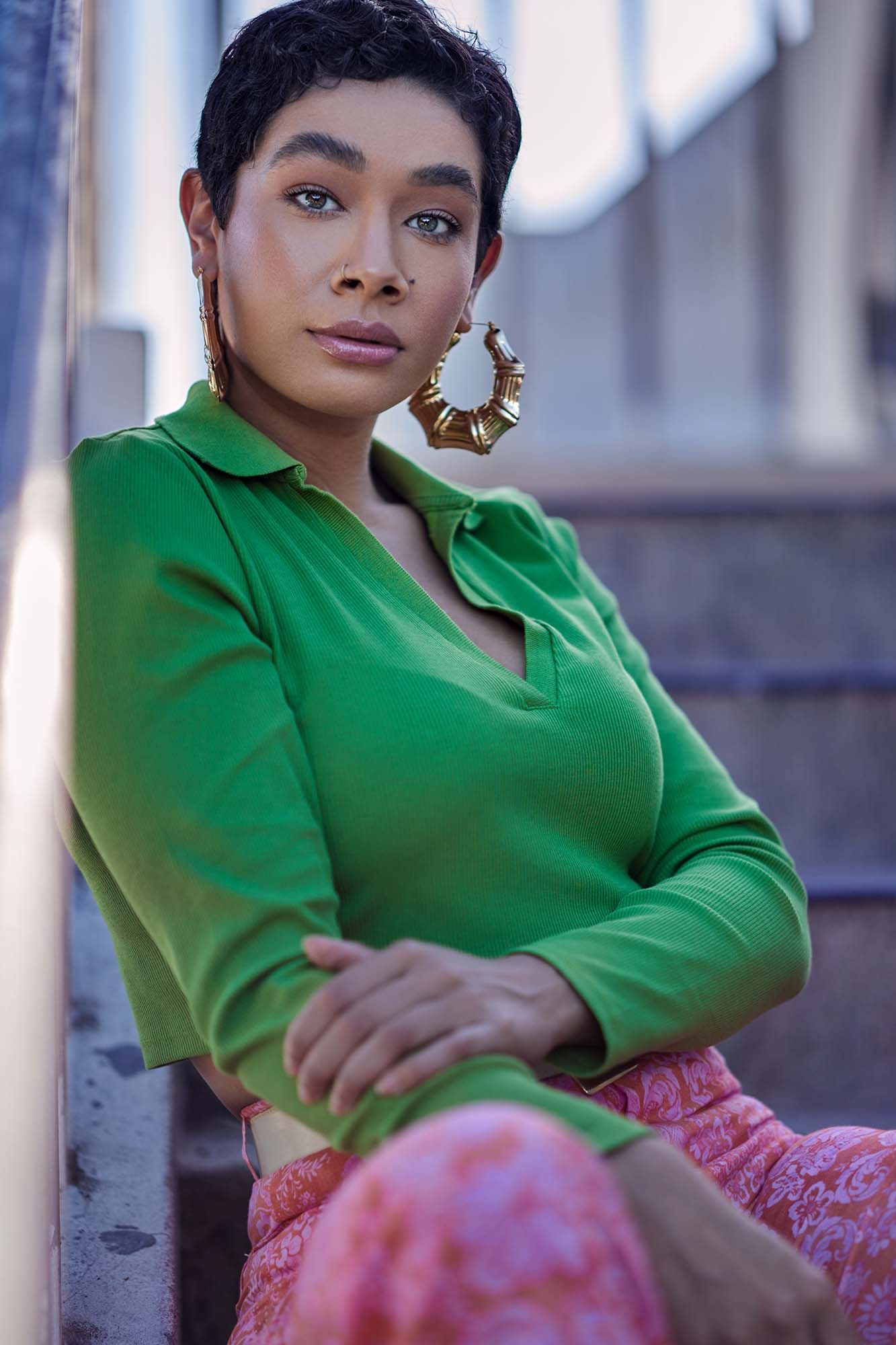 Fashion portrait of a person in a vibrant green top and statement earrings against an urban background.