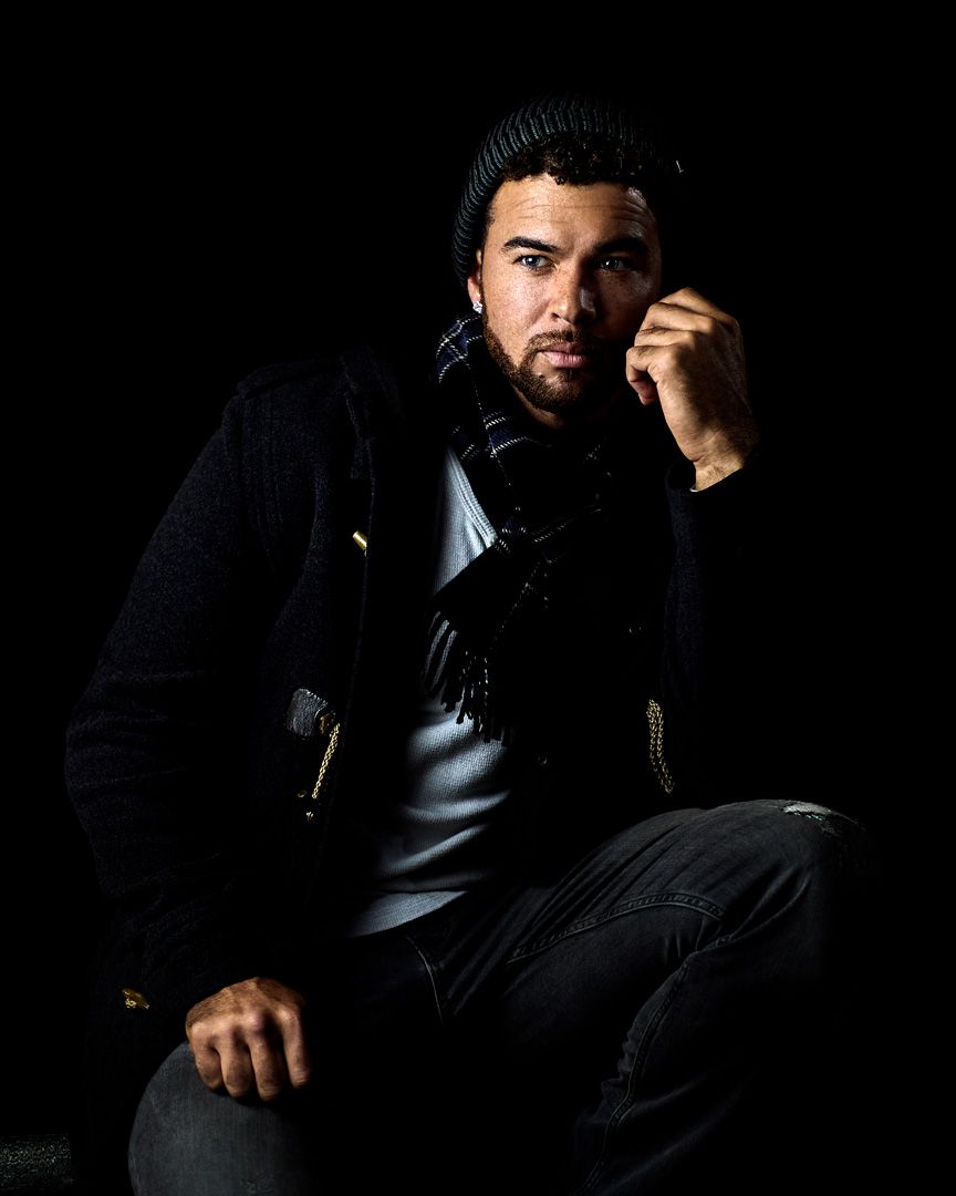 Moody portrait of person in black beanie and jacket against dark background.