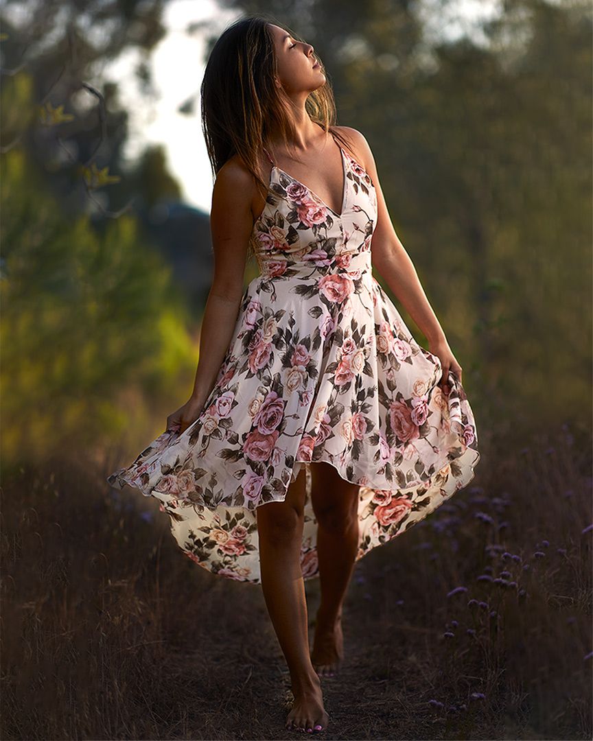 Woman in floral dress twirling outdoors during golden hour photography session.