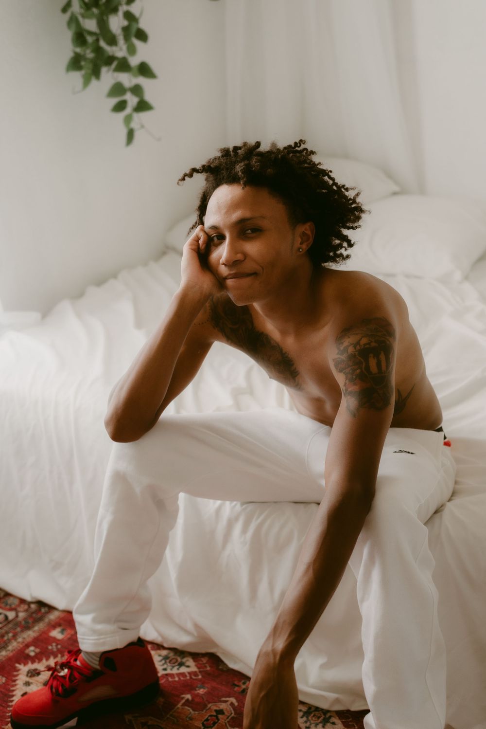 Person relaxing on white bedding wearing red shoes in a bright bedroom setting.