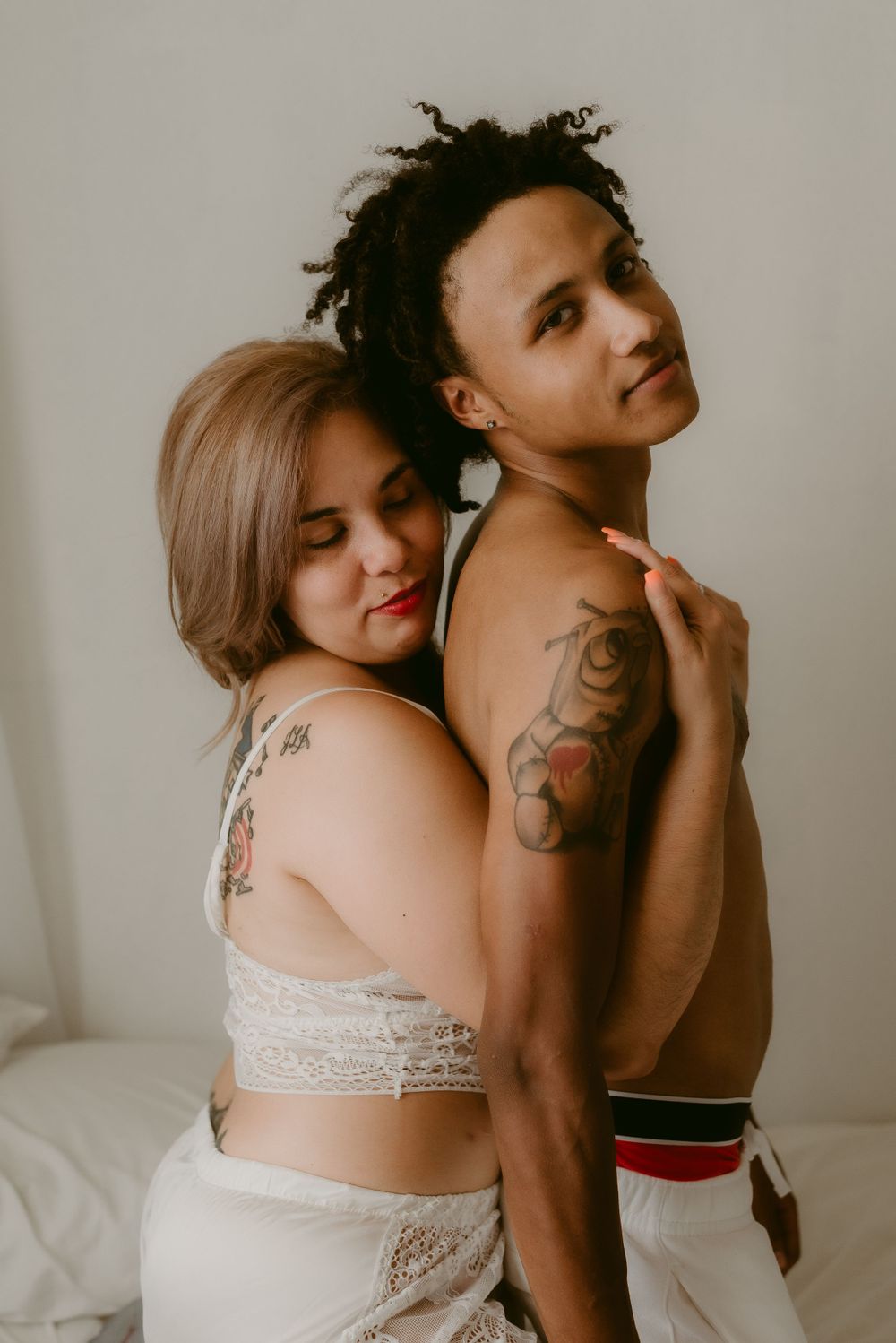 Artistic boudoir photography of a couple in white attire against neutral background.
