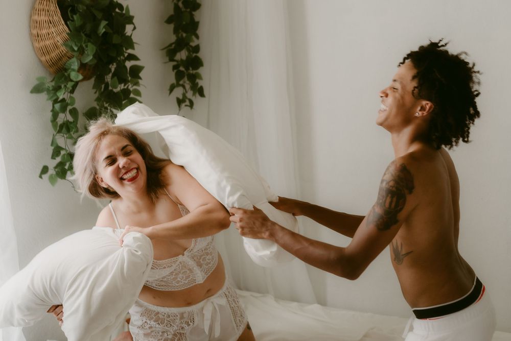 Candid moment of couple having fun with pillows during a bedroom photoshoot.