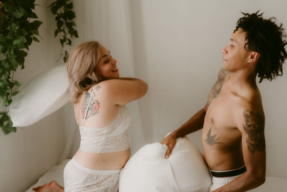 Intimate boudoir photoshoot with couple in white lingerie and underwear on bed with natural lighting.