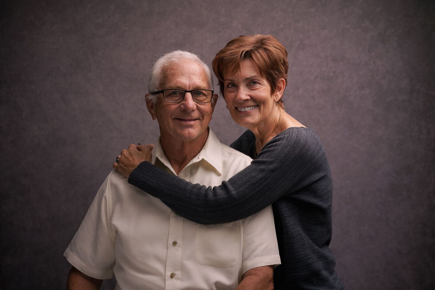 A warm studio portrait of a couple embracing against a dark background.