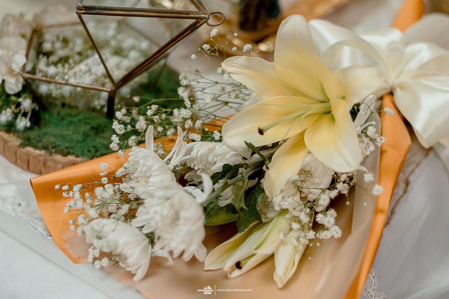 Delicate white lily and baby's breath floral arrangement in geometric glass container.
