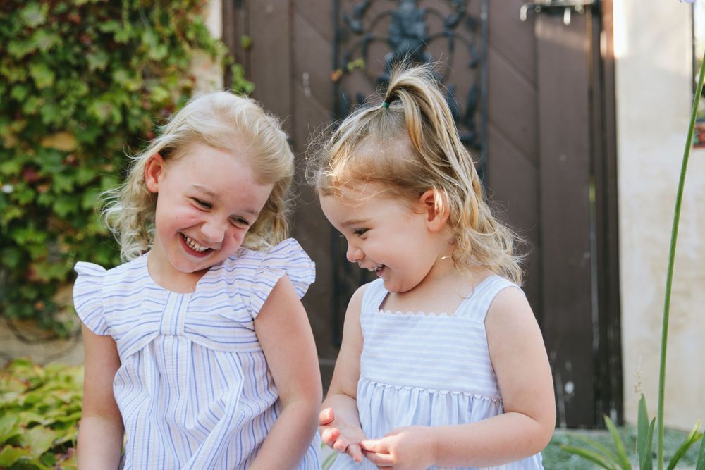 Children in matching blue dresses sharing secrets and giggles in a garden.
