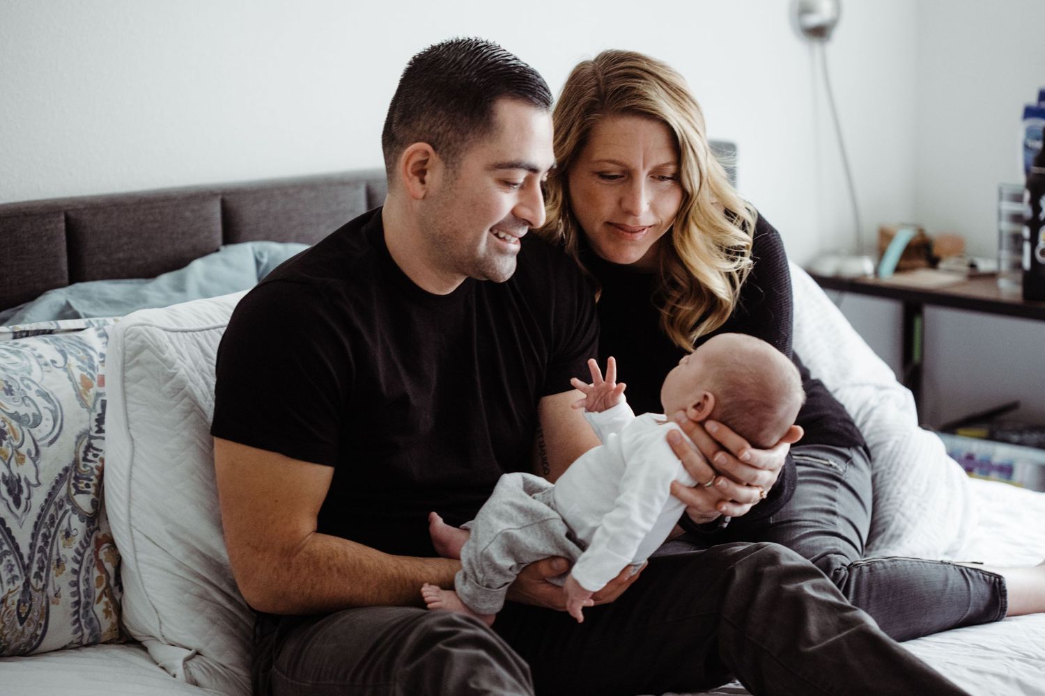 Parents share a quiet moment with their newborn baby on a grey couch.