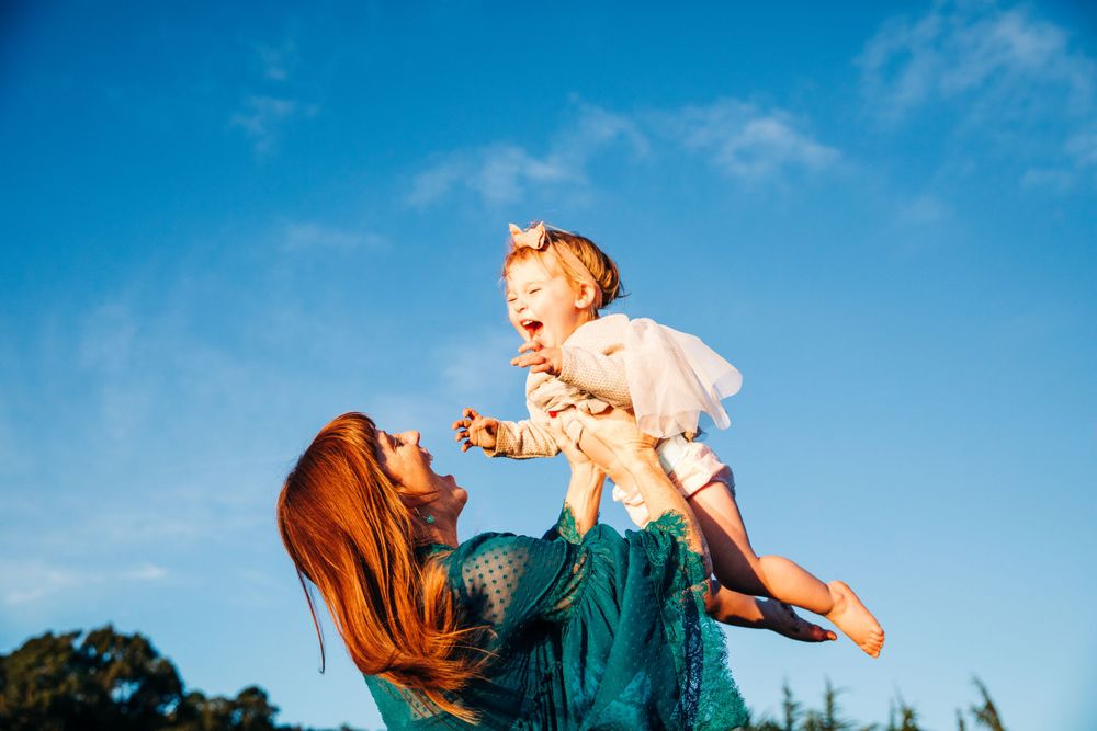 Family plays together against bright blue sky background outdoors.