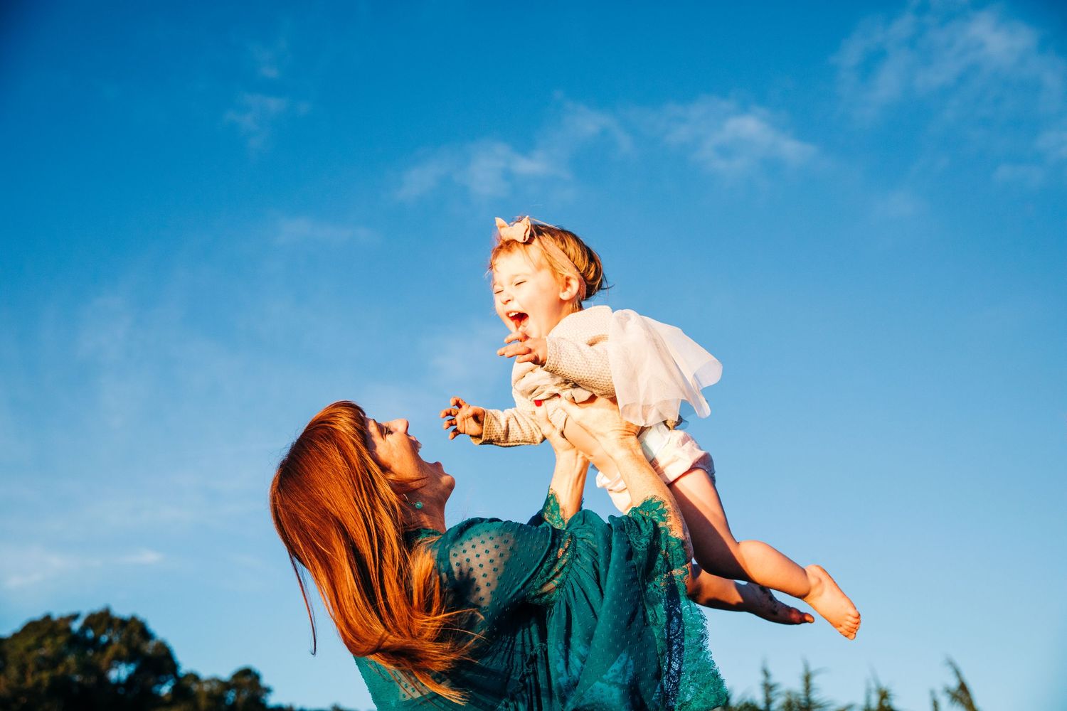 Family plays together against bright blue sky background outdoors.