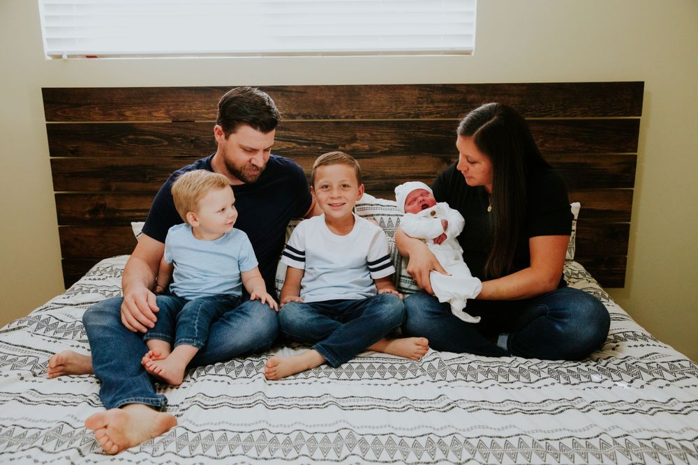 Family relaxing together on a bed with white linens and wooden headboard.