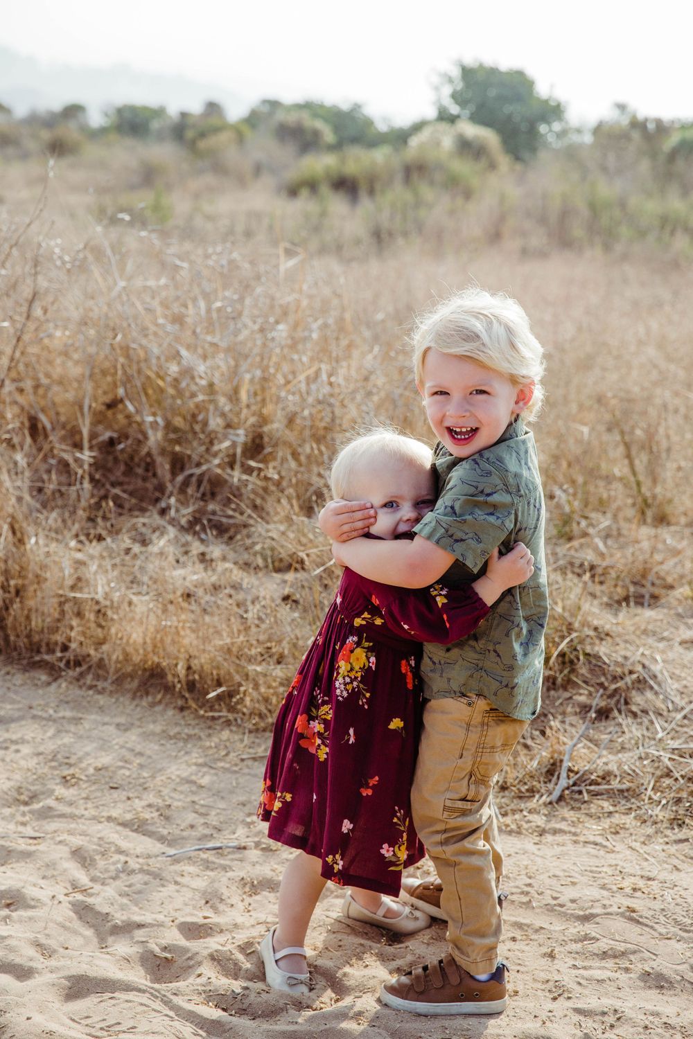 Two small children hugging and playing in a field of dry grass.
