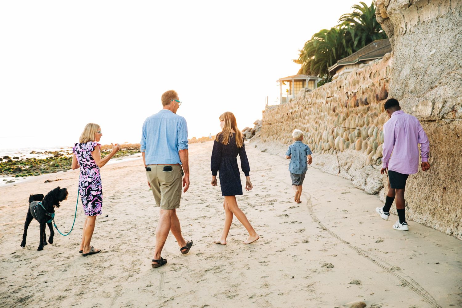 Family and dog walking together on a sandy beach path during golden hour.