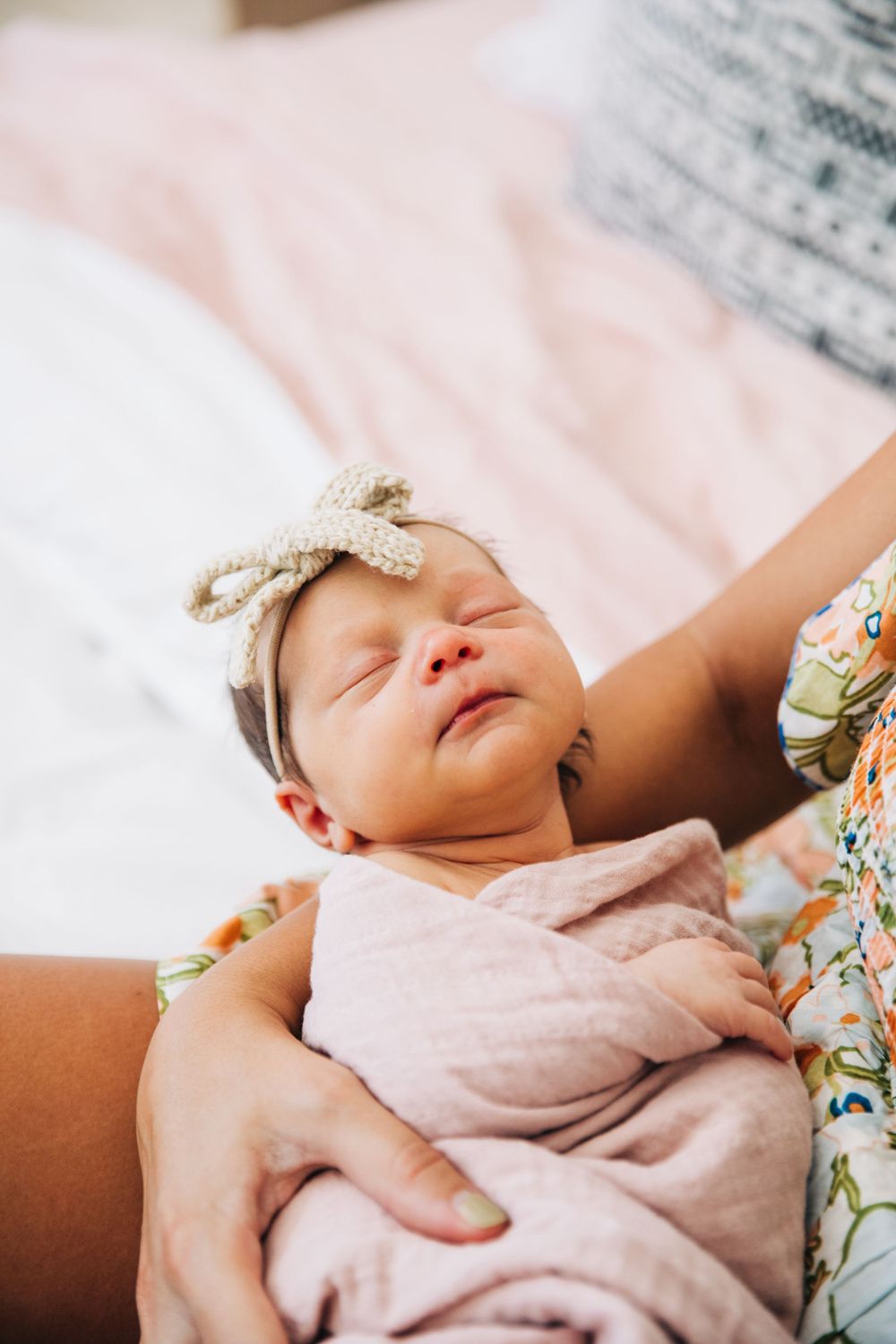 Sleeping newborn wearing pink outfit and bow headband on soft blanket.
