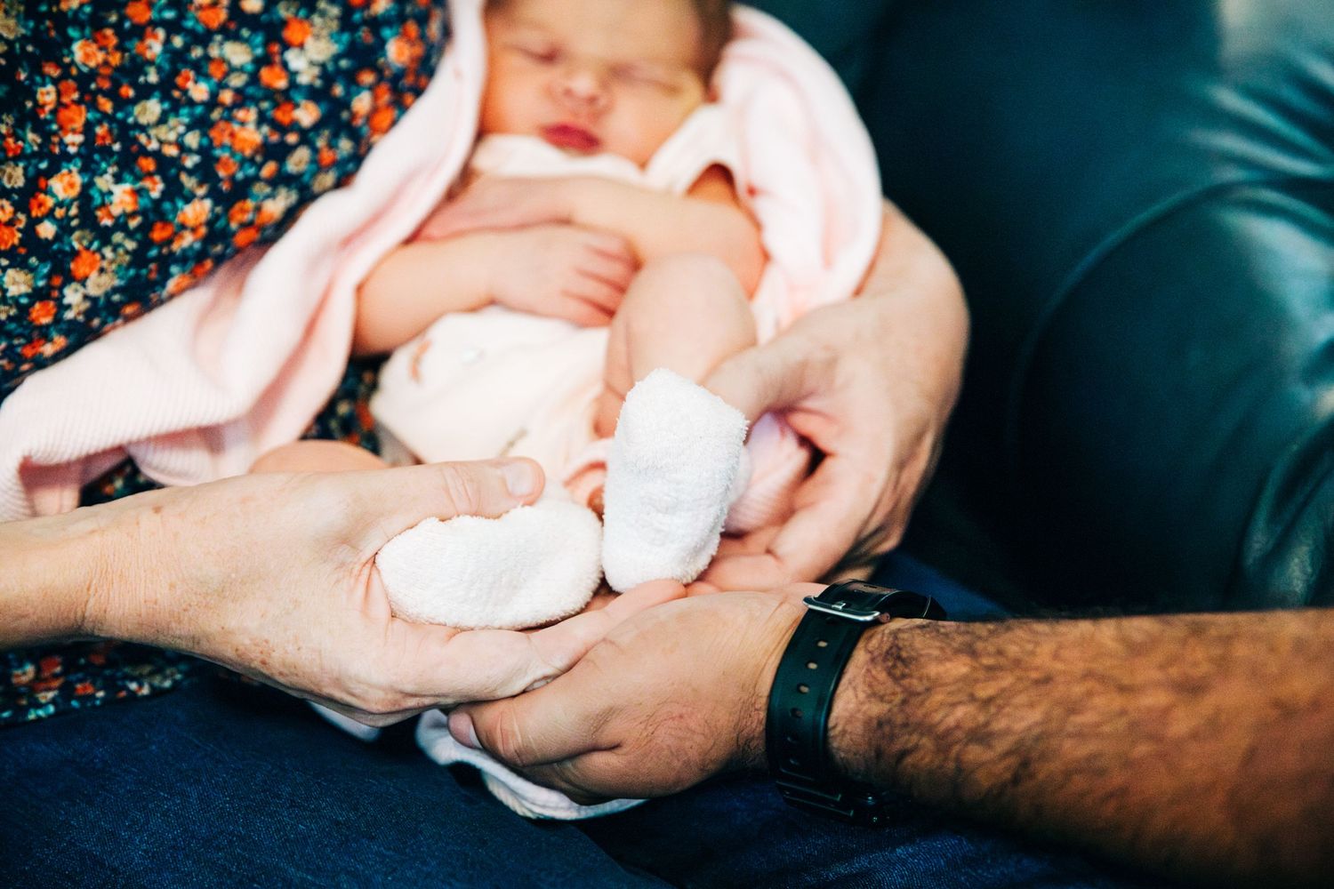 Close-up of gentle hands holding a sleeping newborn baby wrapped in a pink blanket.