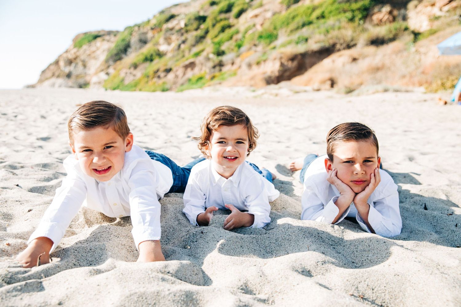 People lying playfully in a row on sandy beach dunes during a photo session.