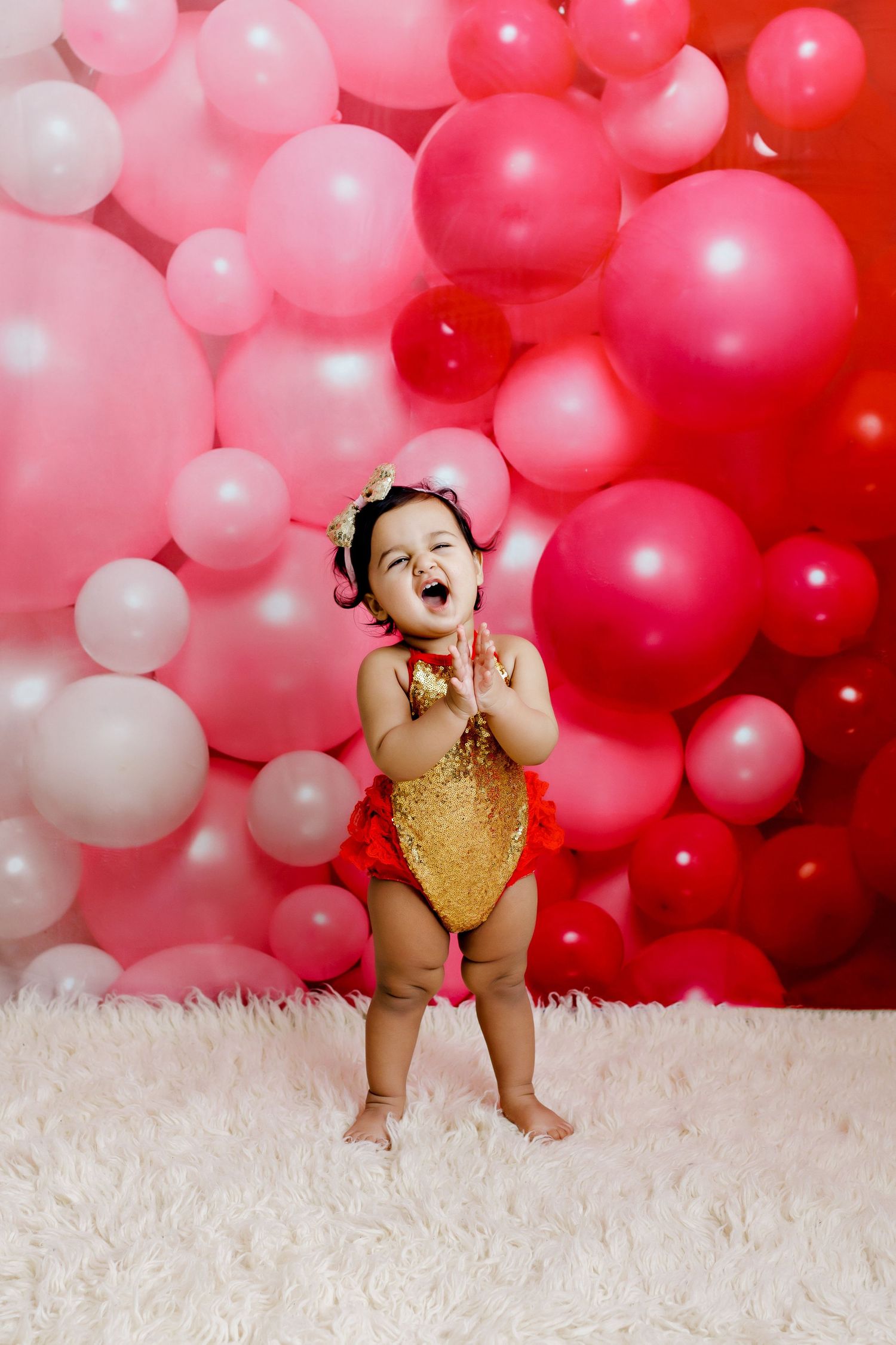 Joyful toddler in gold swimsuit against pink balloon backdrop.