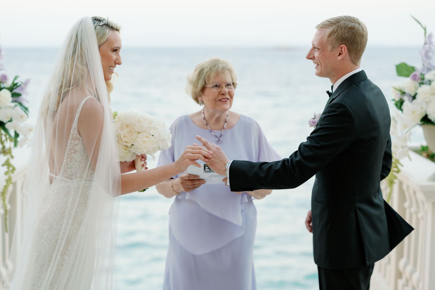 Wedding ceremony exchange of rings at seaside terrace with floral decorations.
