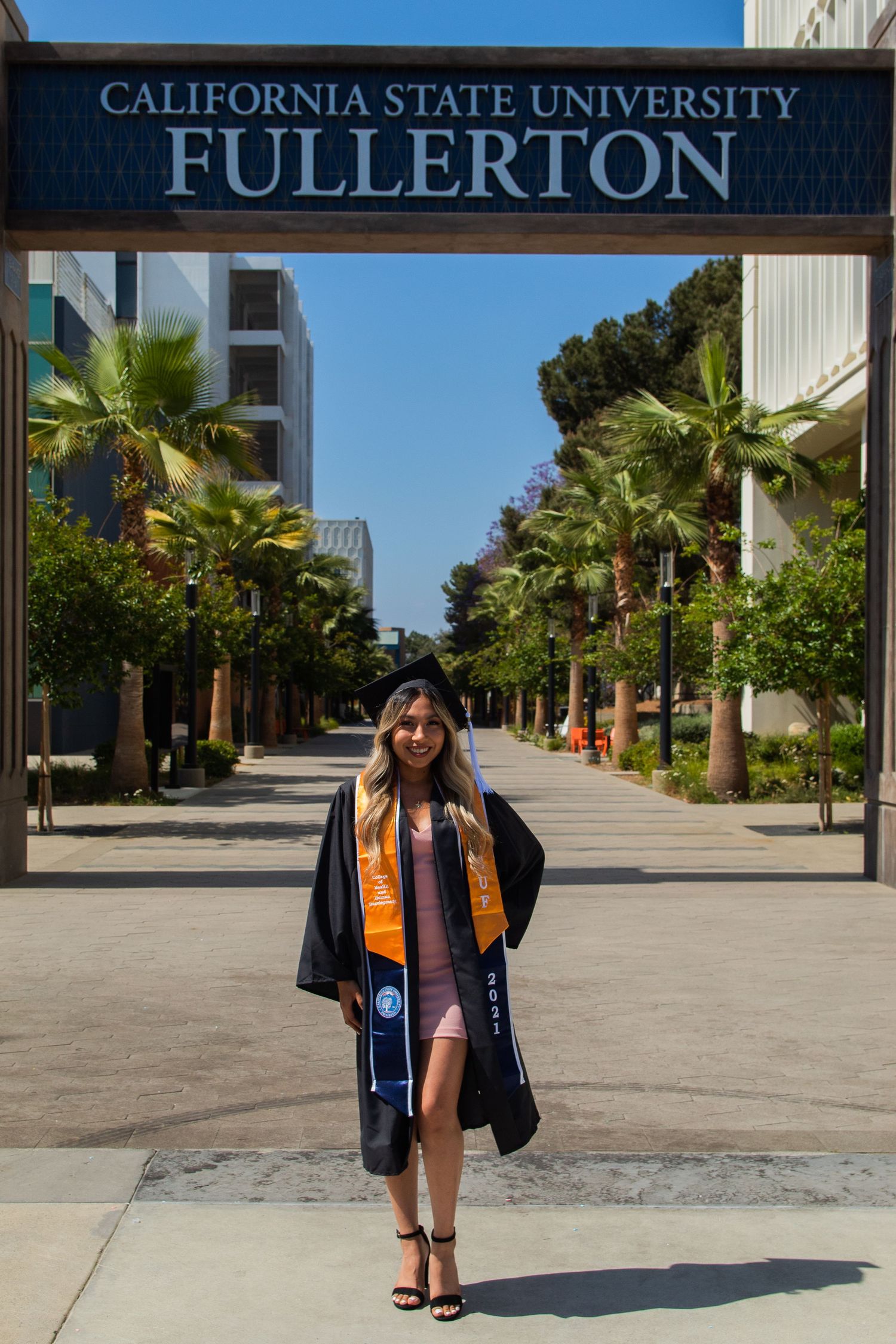 graduating woman posing in front of school sign at UC fullerton in fullerton, ca