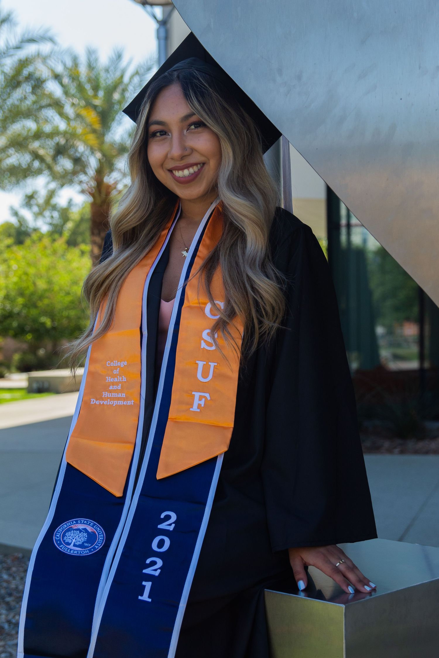 graduating woman posing in front of school sign at UC fullerton in fullerton, ca
