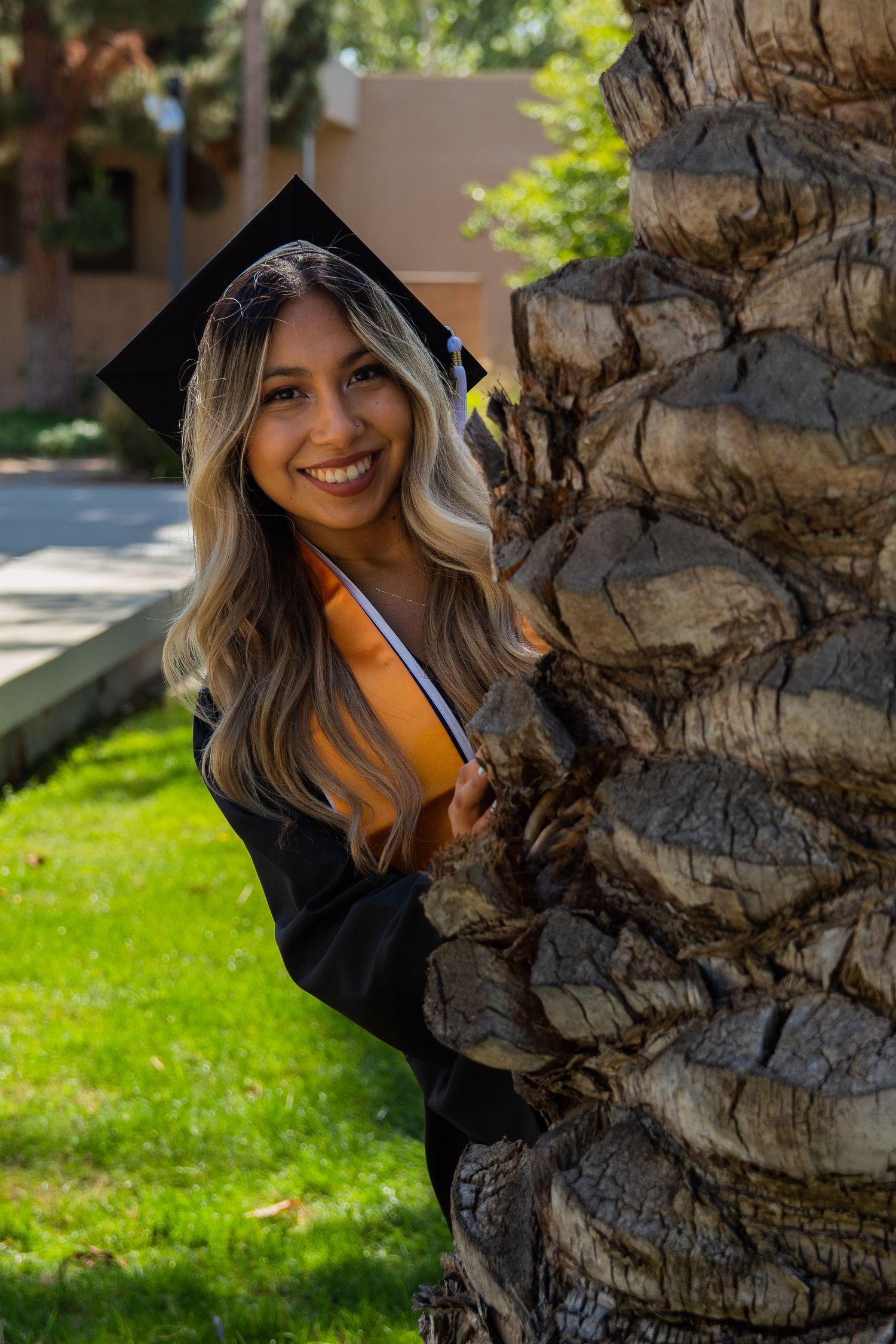 graduating woman peeking around tree at UC fullerton in fullerton, ca