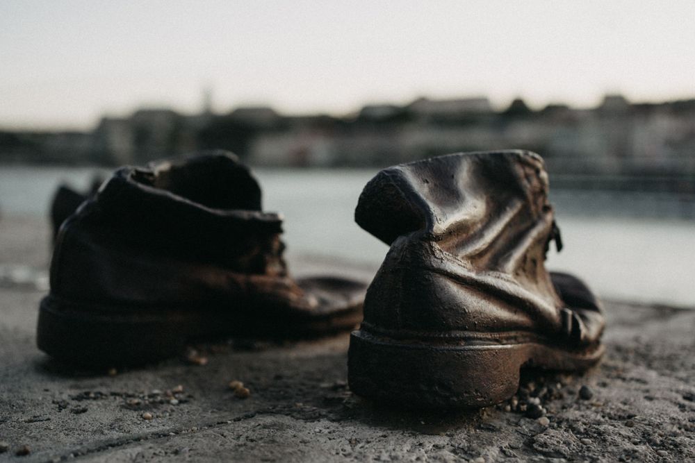 Old worn boots placed near water's edge with blurred background.