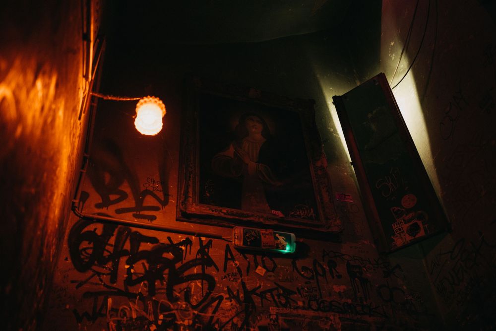 Dimly lit underground corridor with red ambient lighting and graffiti on concrete walls.