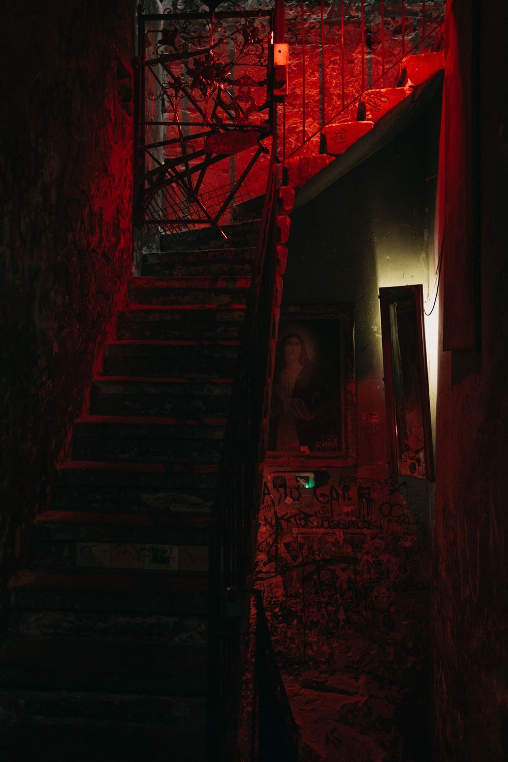 Abandoned staircase bathed in red light with graffiti-covered walls creating an urban atmosphere.