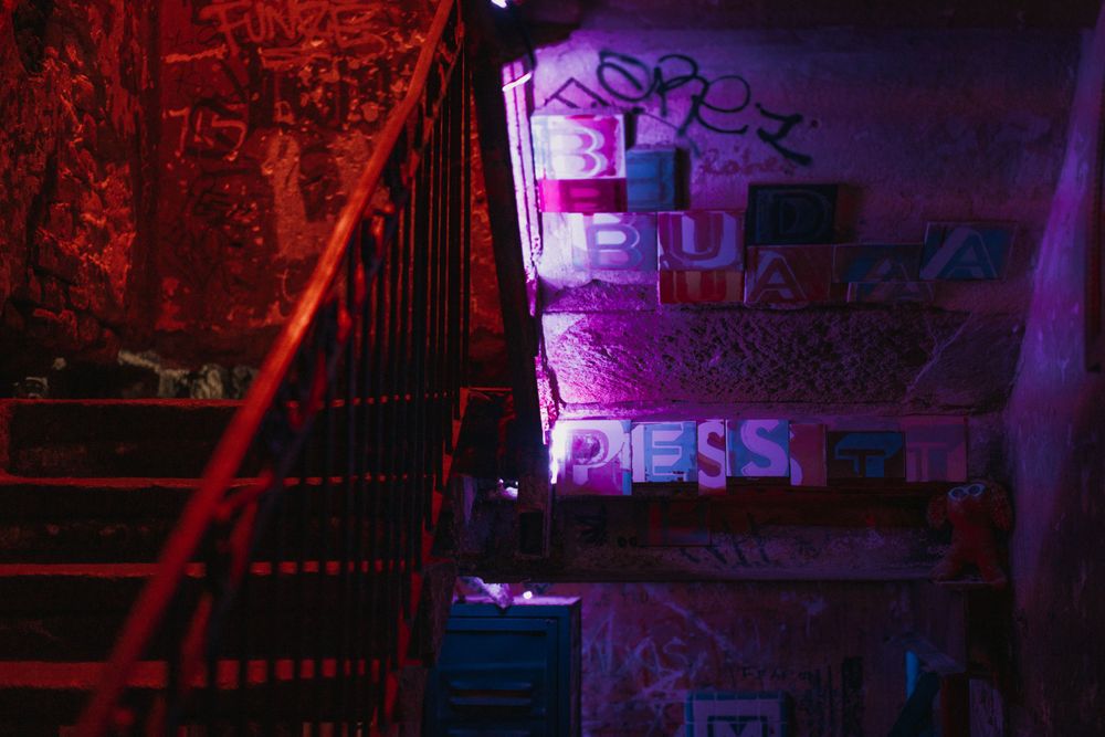 Industrial stairwell with purple and red lighting casting shadows on graffiti-marked walls.