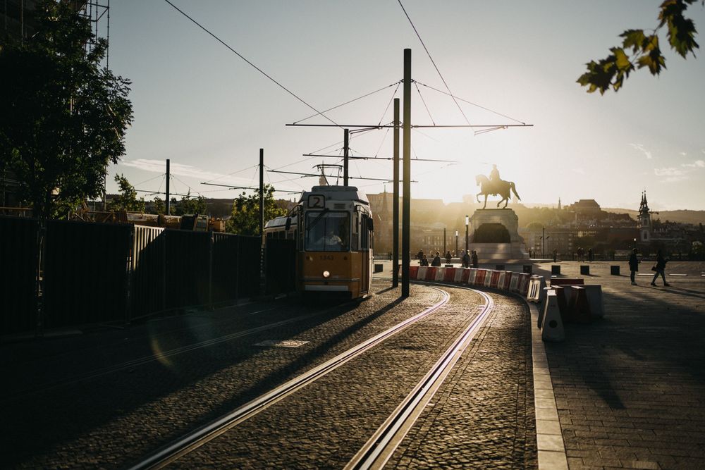 Empty tram tracks leading into the distance during golden hour with urban surroundings.