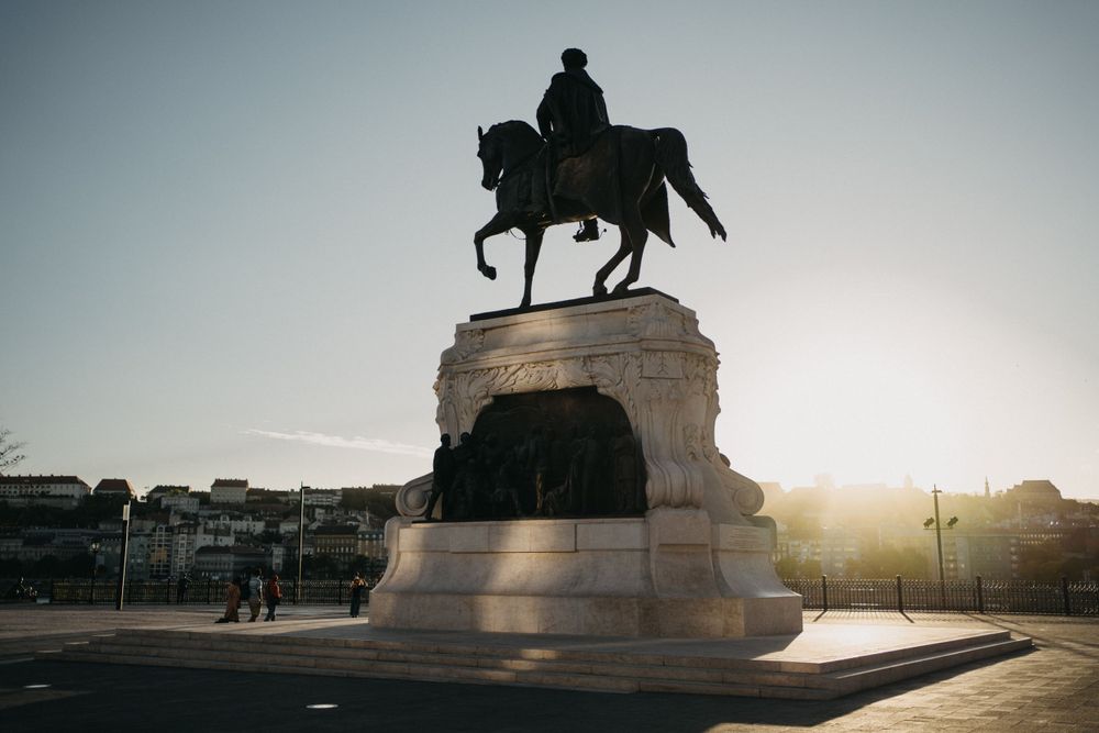 Silhouetted equestrian statue at sunset with dramatic sky backdrop.