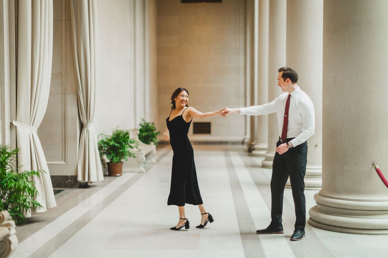 A couple dancing together in an elegant hallway with classical columns and curtains.