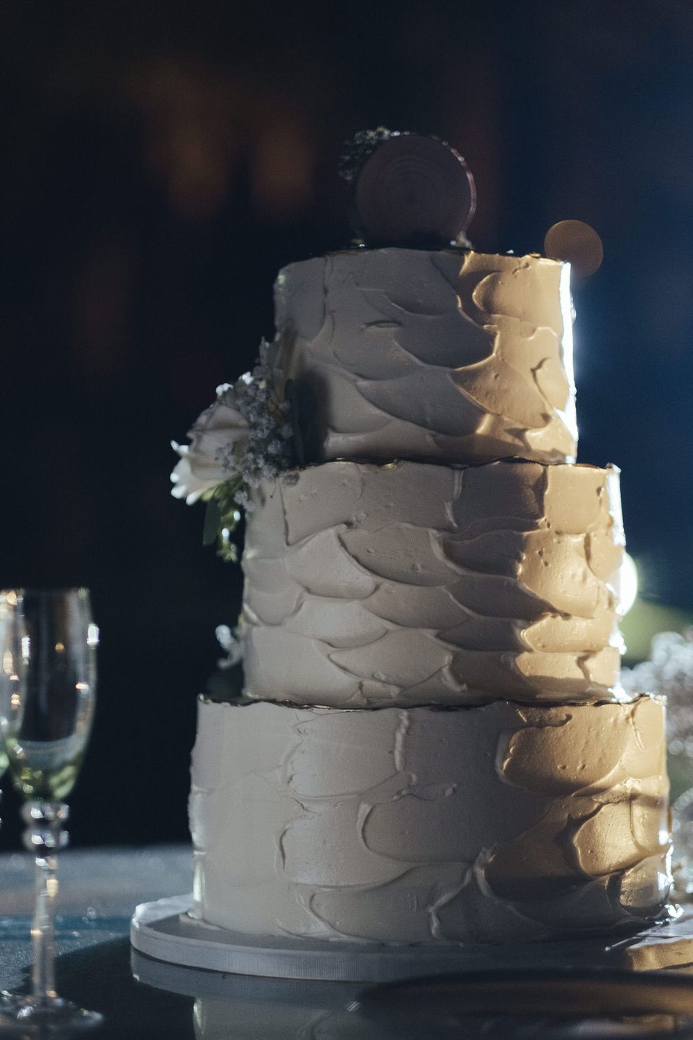 Elegante bolo de casamento branco com camadas de glacé texturizado, exibido sobre um fundo escuro.