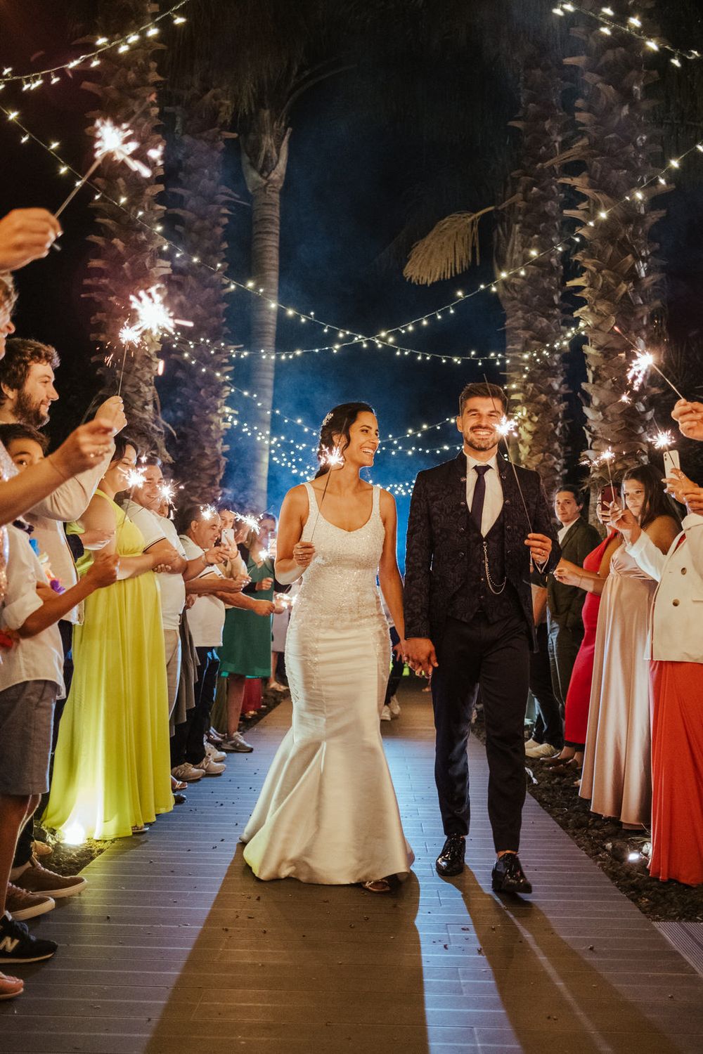 A festa de casamento celebra com velas de faísca no deck exterior sob luzes de cordão.
