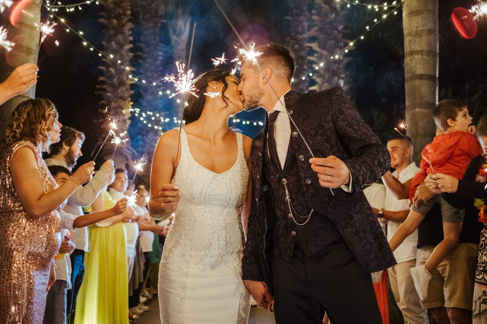 Os convidados do casamento seguram velas de faísca, criando uma atmosfera mágica de celebração noturna sob luzes de cordão.