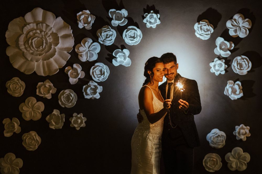 Uma iluminação dramática destaca as decorações de parede com flores de papel branco num evento elegante.
