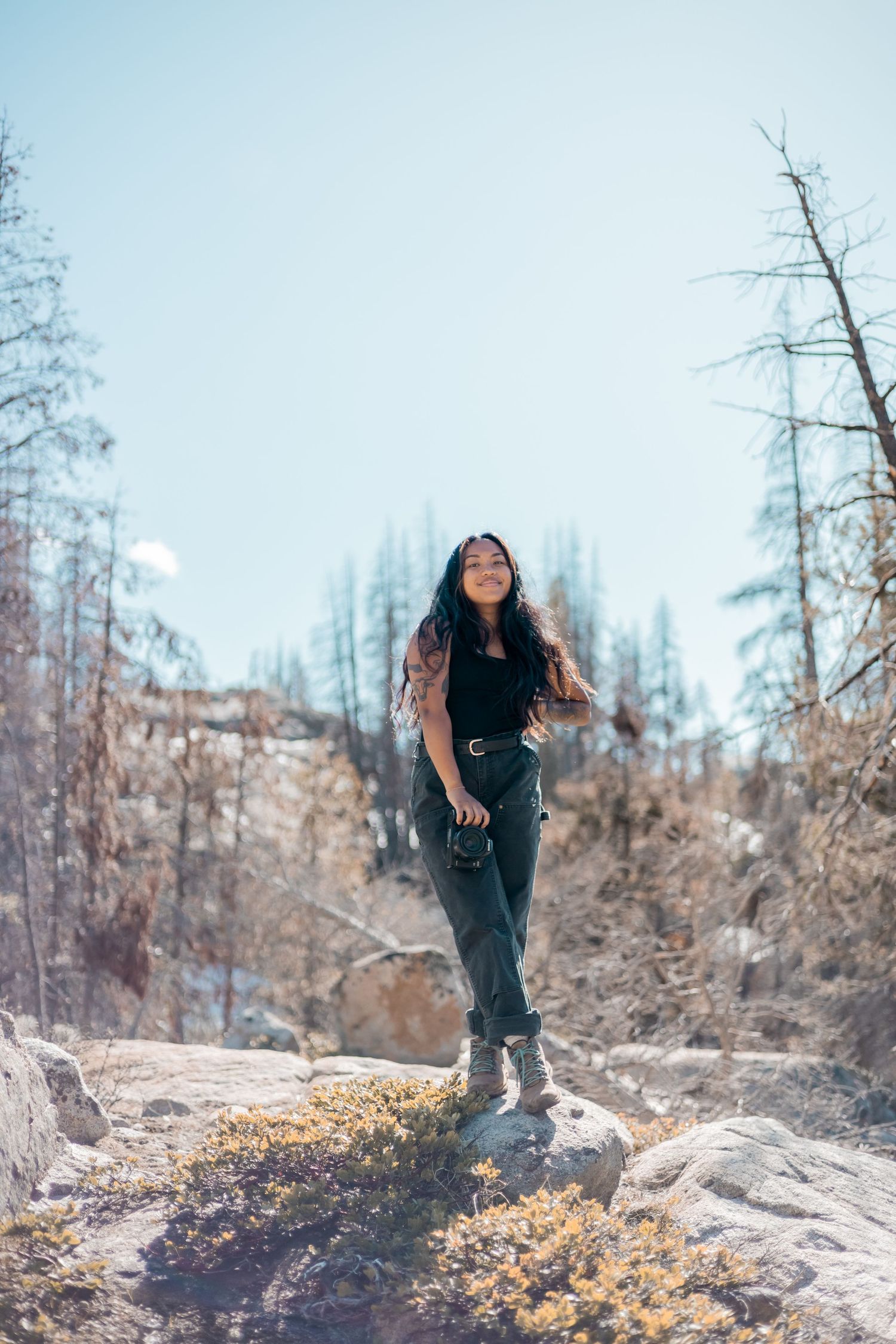 Woman in black outfit standing on rocky terrain against mountain backdrop.