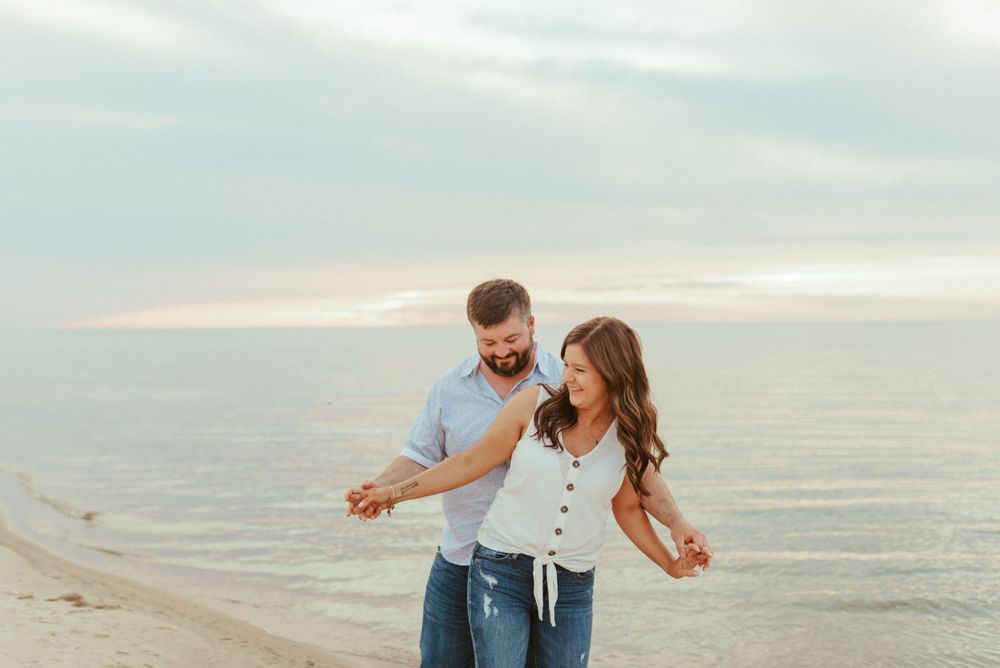 A playful couple dancing together on a beach at dusk.