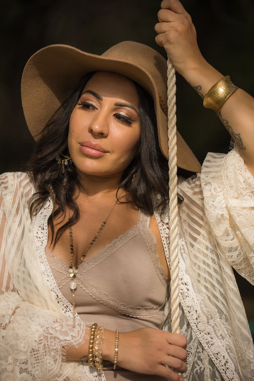 A bohemian style portrait featuring lace, jewelry and a wide-brimmed hat in warm lighting.