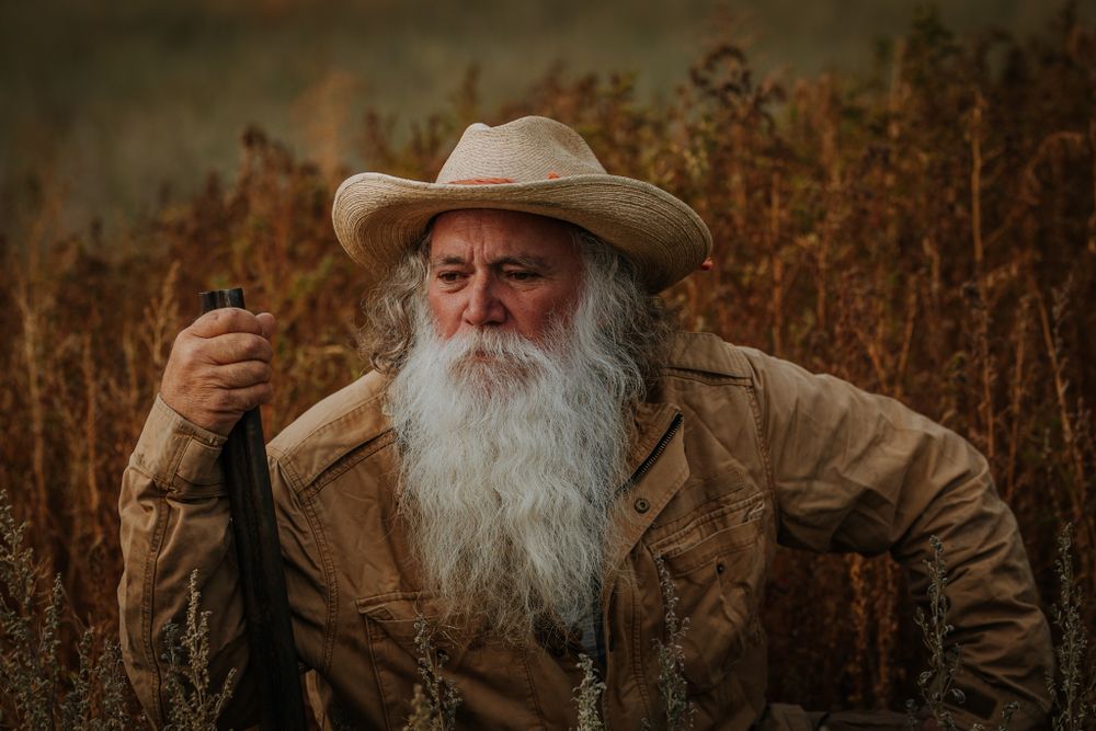 A rustic portrait in golden light shows weathered workwear against autumn vegetation.