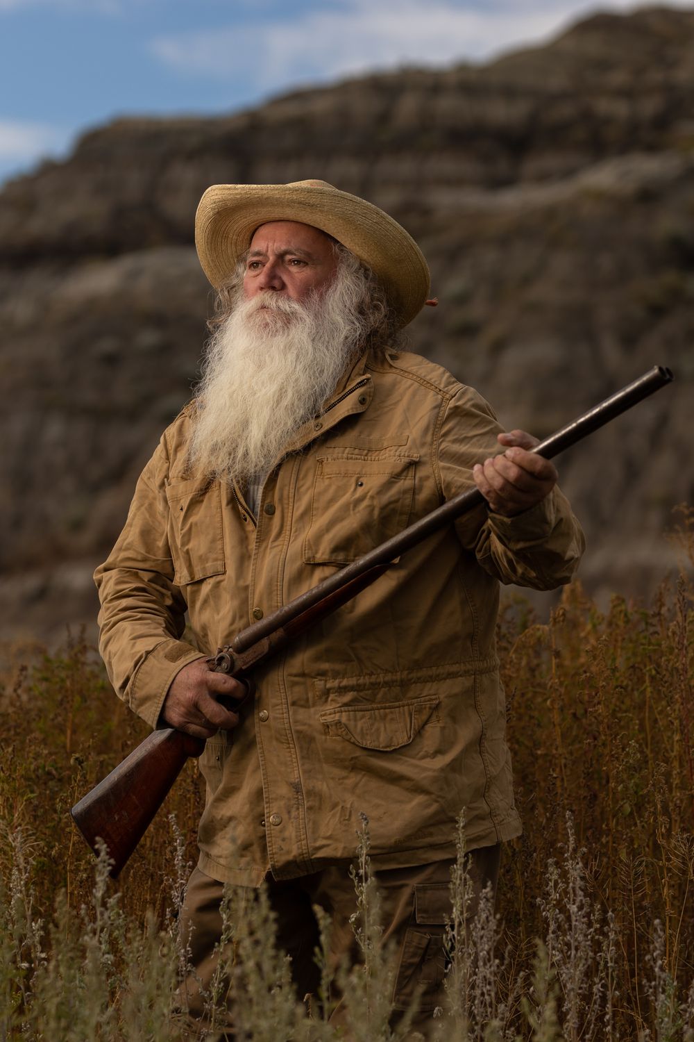 A western-styled figure holds a vintage rifle against a rocky desert landscape.