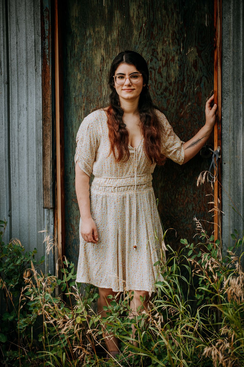 Portrait in cream vintage dress against rustic metal wall with wild plants.