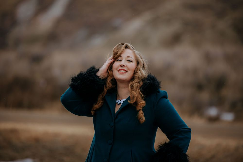 A joyful outdoor portrait of someone in a navy coat with fur trim against a brown backdrop.