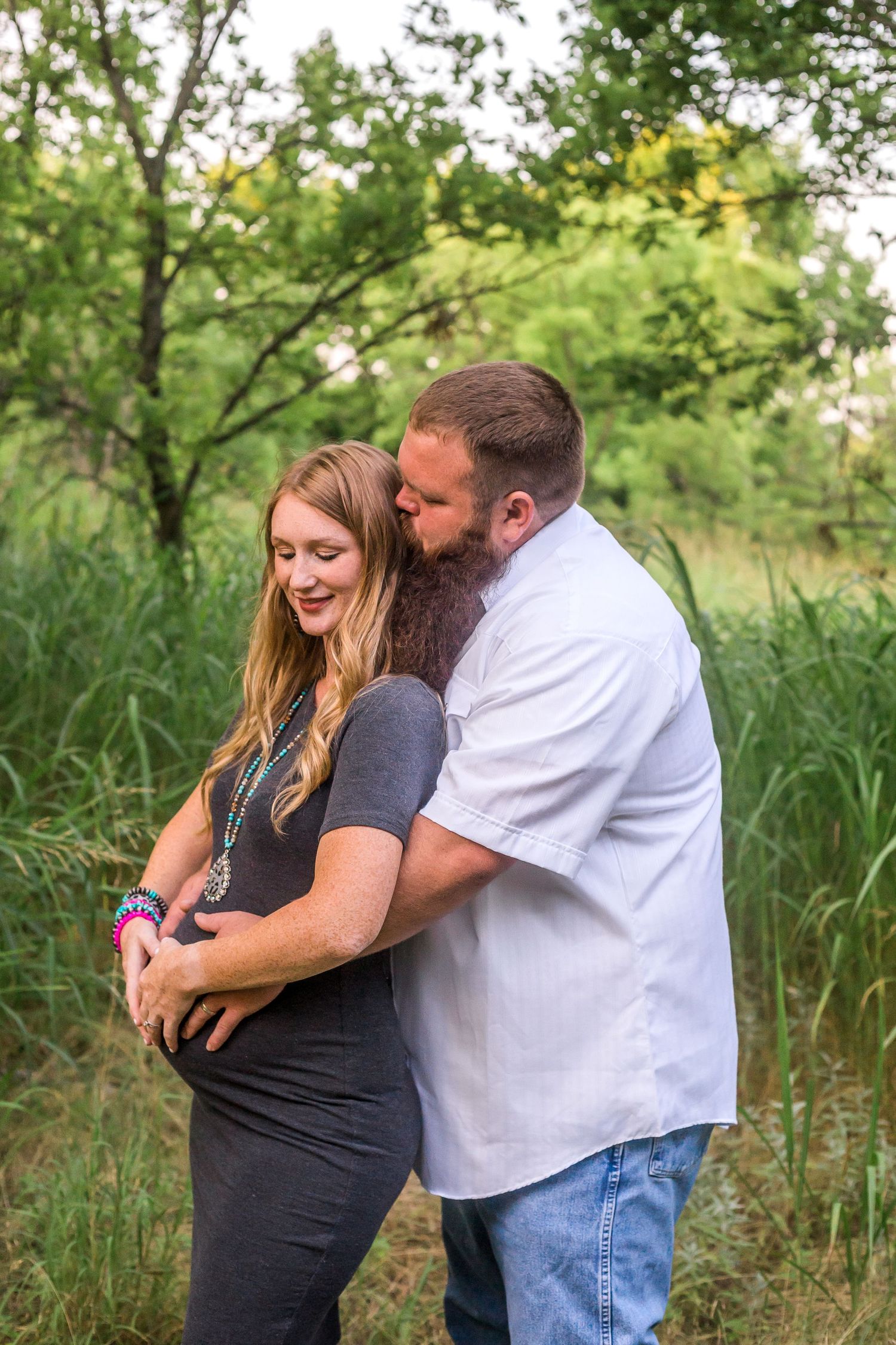 Intimate maternity photo of couple embracing in tall grass.