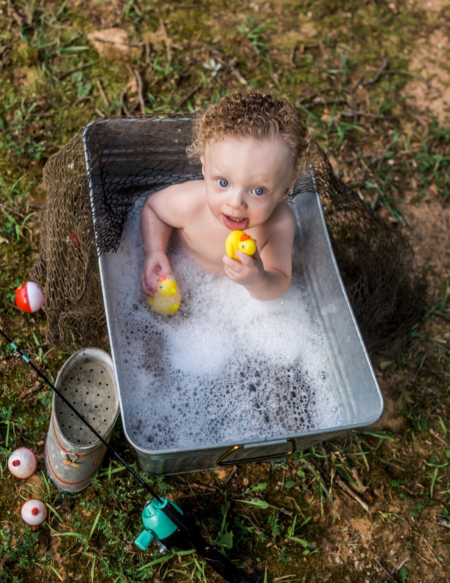 Baby playing with rubber ducks in a metal tub bath outdoors.