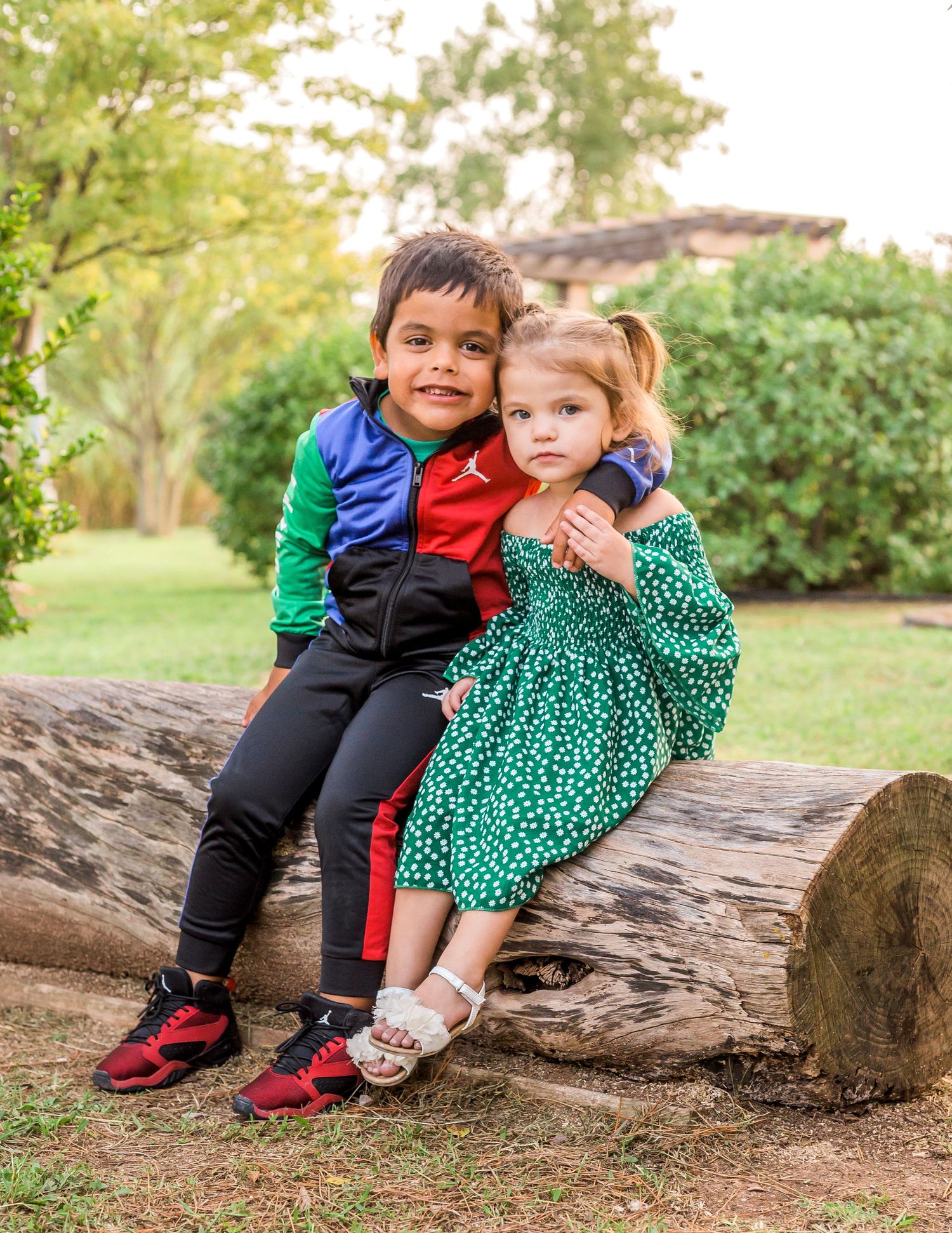 Two children sit together on rustic log in garden setting during summer.