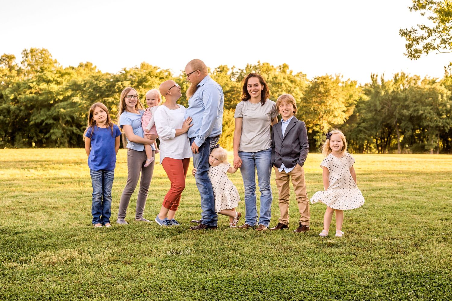 Group photo of a large family standing together in a grassy field at sunset.