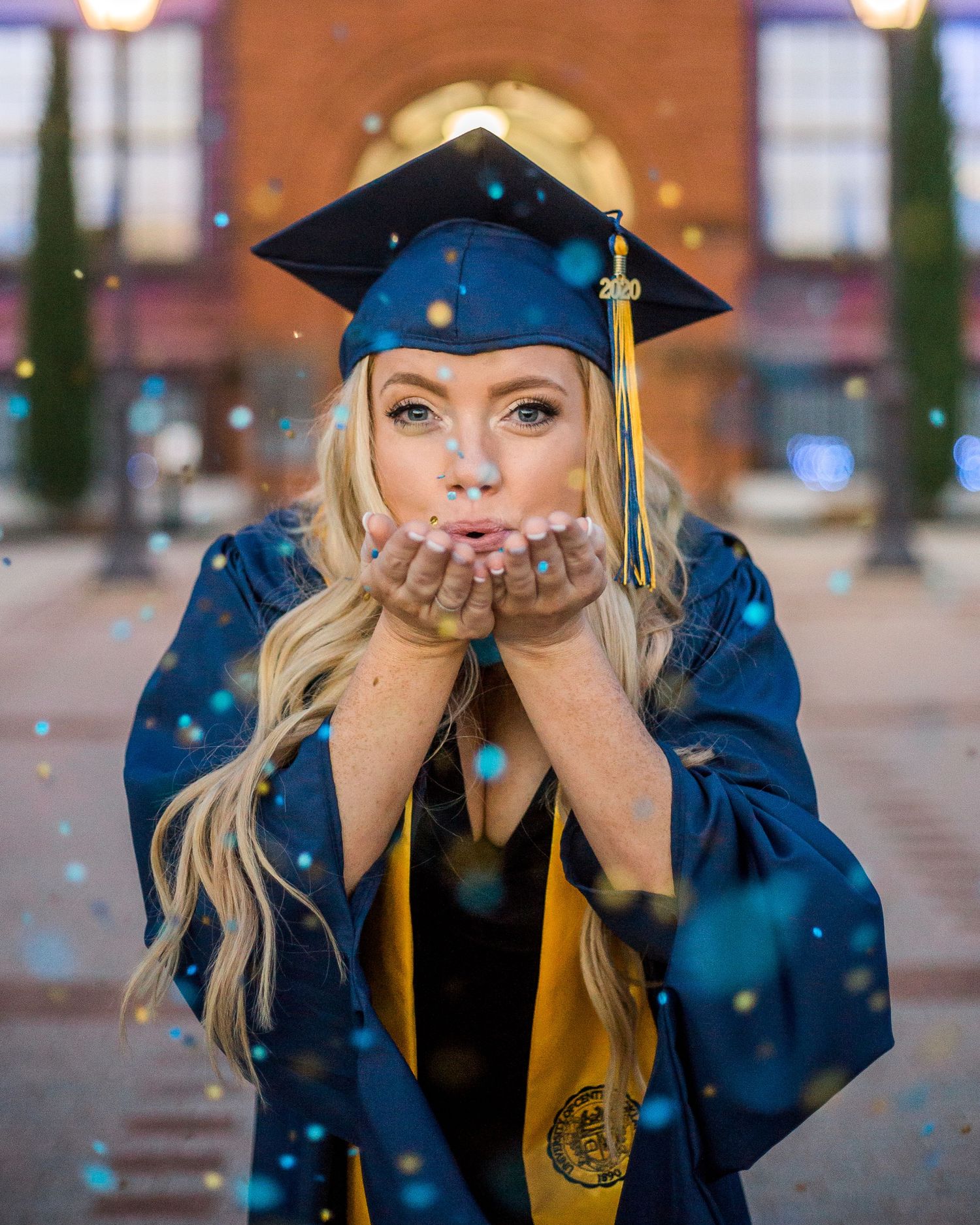 Graduate in blue cap and gown blowing glitter in celebration.