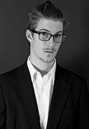 Professional black and white portrait of a young man in suit and glasses.